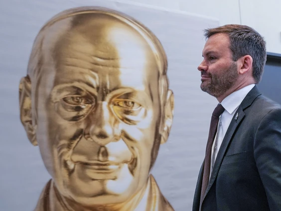 A man in a suit walking past a large golden statue of a smiling face.