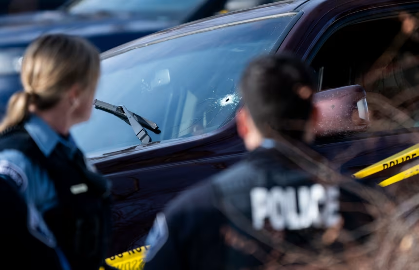 A police scene with two officers examining a vehicle with a bullet hole in the windshield.